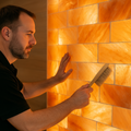 Technician dry-dusting a glowing pink Himalayan salt wall with a soft brush.