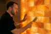 Technician dry-dusting a glowing pink Himalayan salt wall with a soft brush.